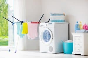 White washing machine and dryer in a laundry room with clothesline hanging. Also, an open glass door ensures proper ventilation to prevent mould and mildew growth in your laundry room.