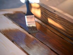 Applying stain to recycled timber joinery with a brush in a close-up shot.