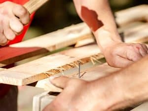 Close-up of hands hammering nails into recycled timber joinery, showcasing the construction process.