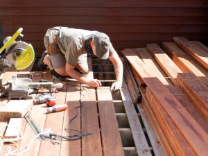 Contractor installing wooden deck boards with tools, highlighting deck permit requirements for construction and renovation projects.