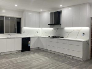 Modern kitchen renovation on a budget featuring sleek white cabinetry, marble backsplash, and under-cabinet lighting in a small space.