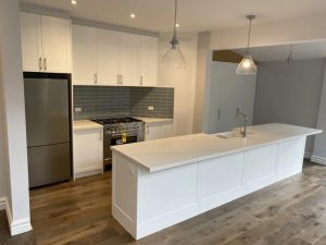 Bright kitchen showcasing modern kitchen cupboard designs with white cabinetry, a large island, and pendant lighting.