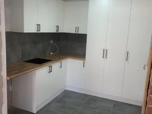 Small L-shaped kitchen renovation on a budget with white cabinets, wood countertops, and modern black handles.